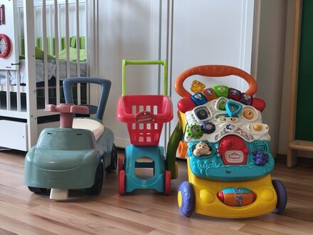 Rutschauto, Spielzeug-Einkaufswagen und Lauflernwagen nebeneinander auf dem Holzboden