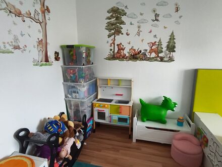 Kinderspielküche neben Stapelboxen mit Spielsachen und einem Korb voller Kuscheltiere
